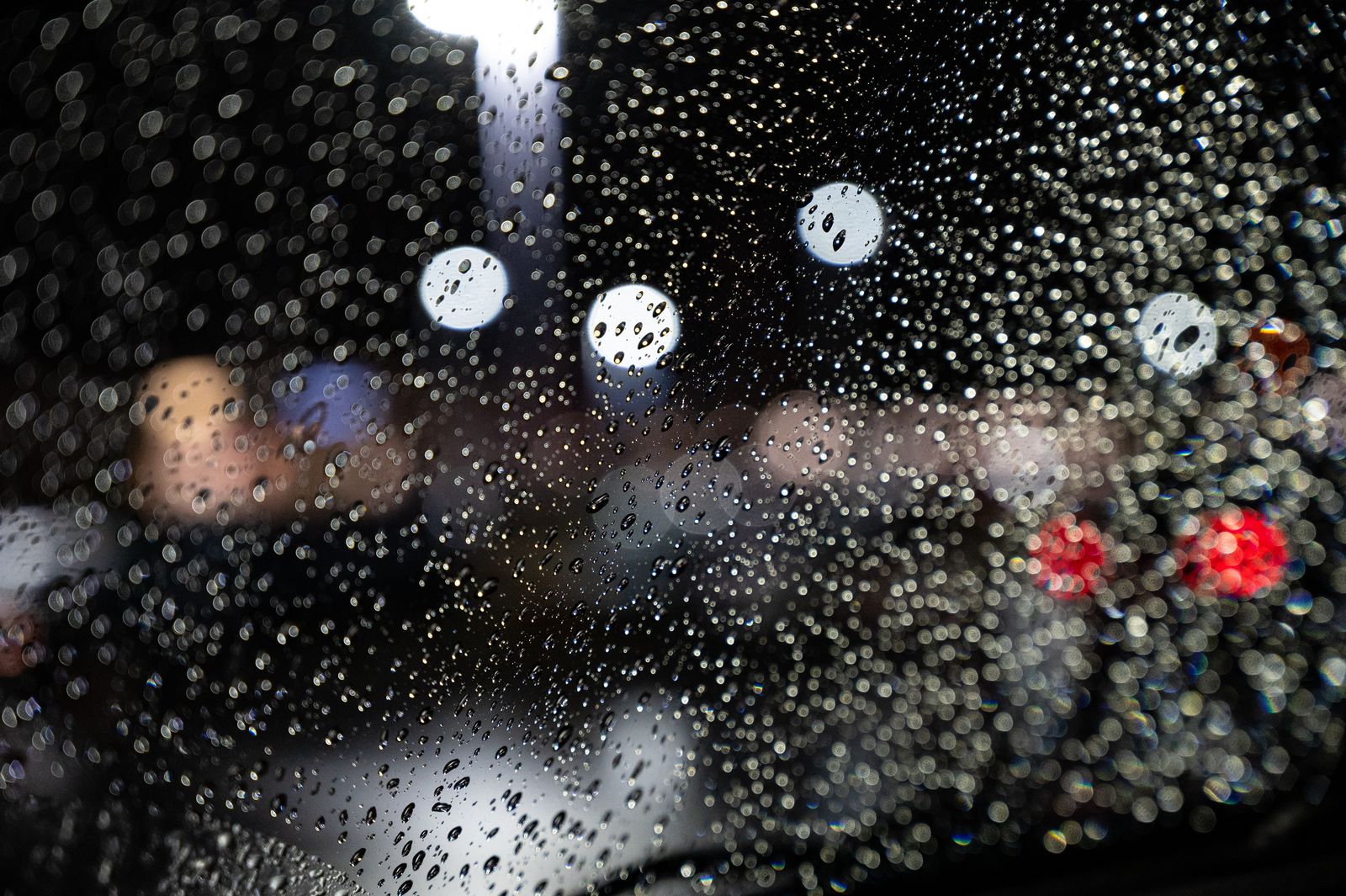 Clear raindrops on car windshield with colorful bokeh lights in the background during night time.