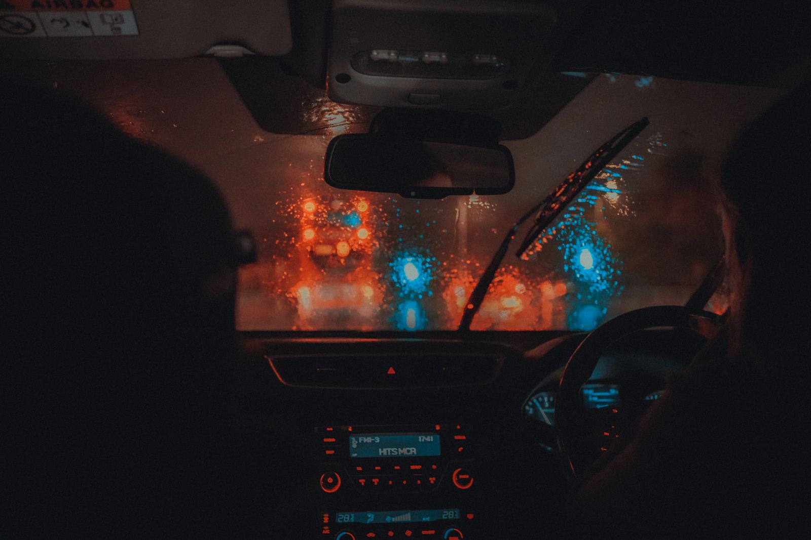 Cinematic view from a car interior driving through Manchester at night in the rain.