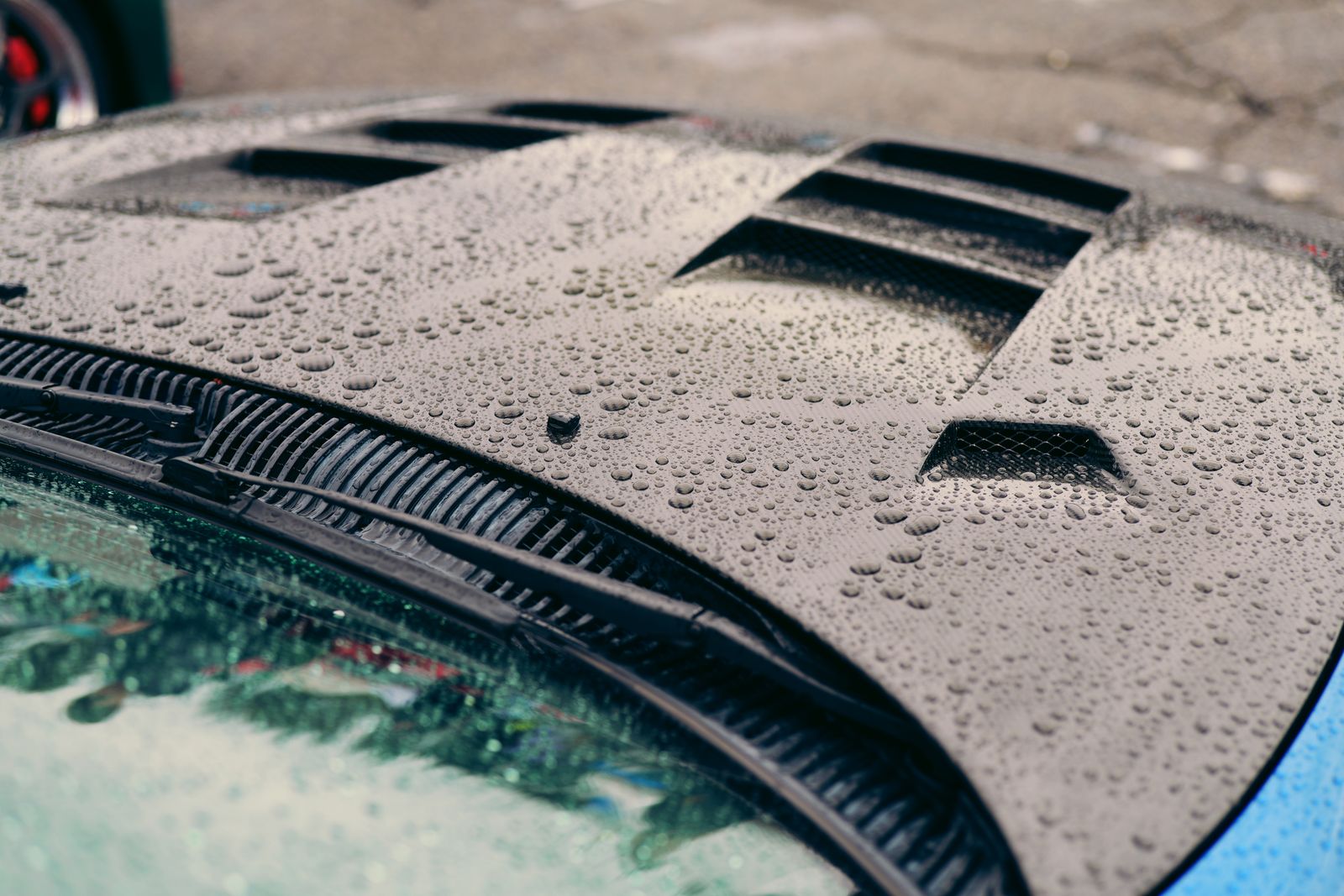 Raindrops on a sleek car hood create a textured pattern, emphasizing automotive design.
