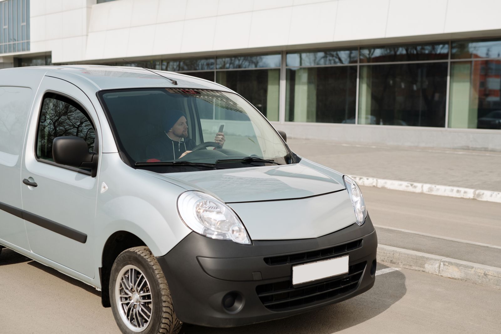 A delivery driver in a van using a smartphone while parked outside a modern building.