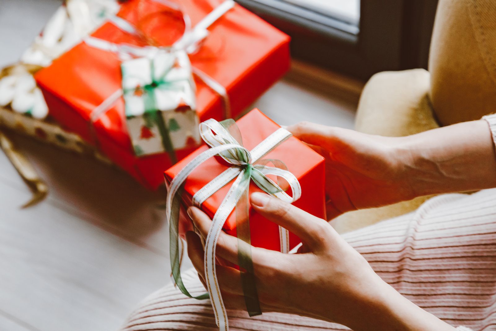 Close-up of hands holding a wrapped Christmas gift tied with ribbon, capturing the festive mood.