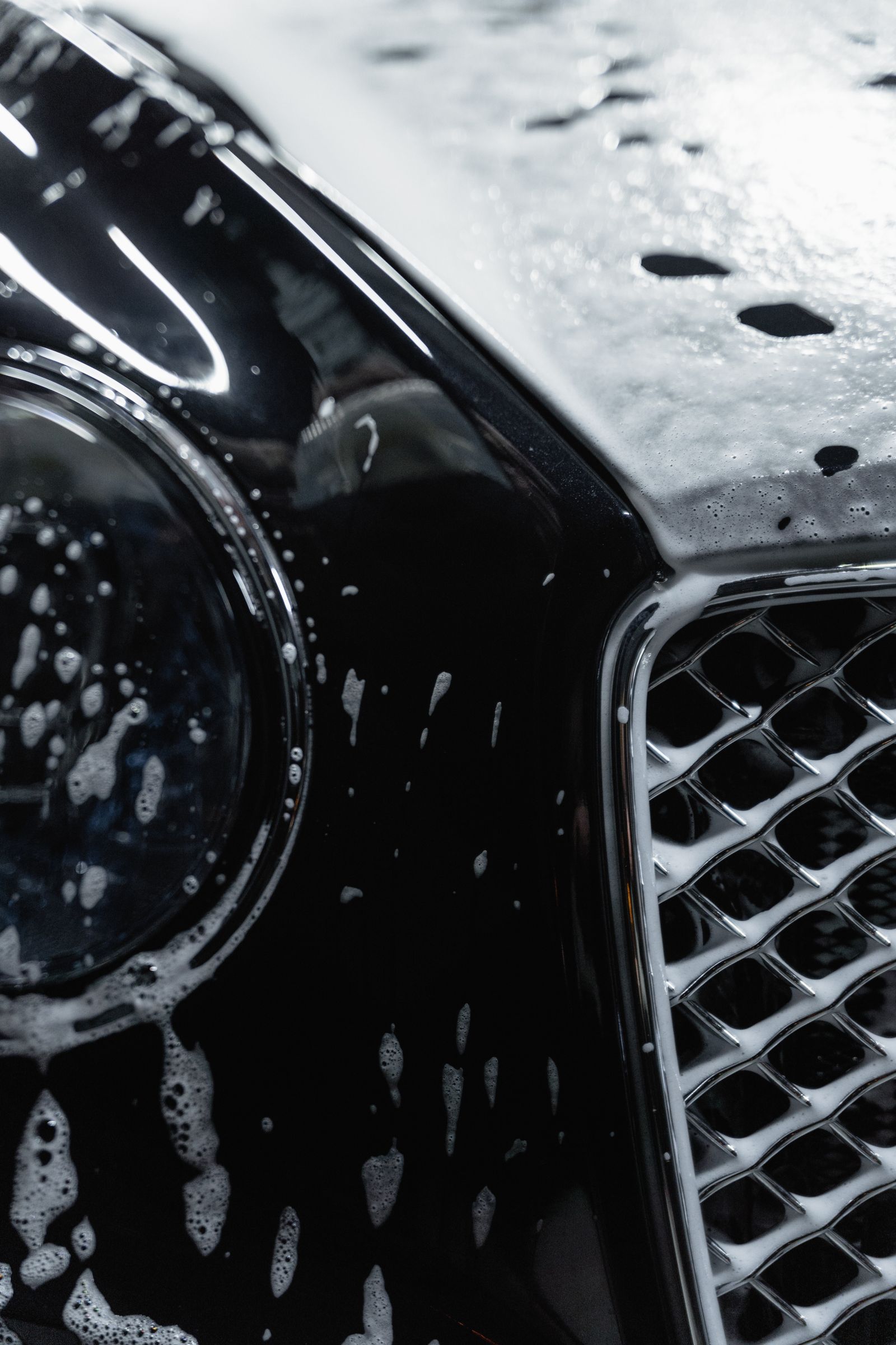 Detailed view of a luxury black car covered with soap suds during a wash.