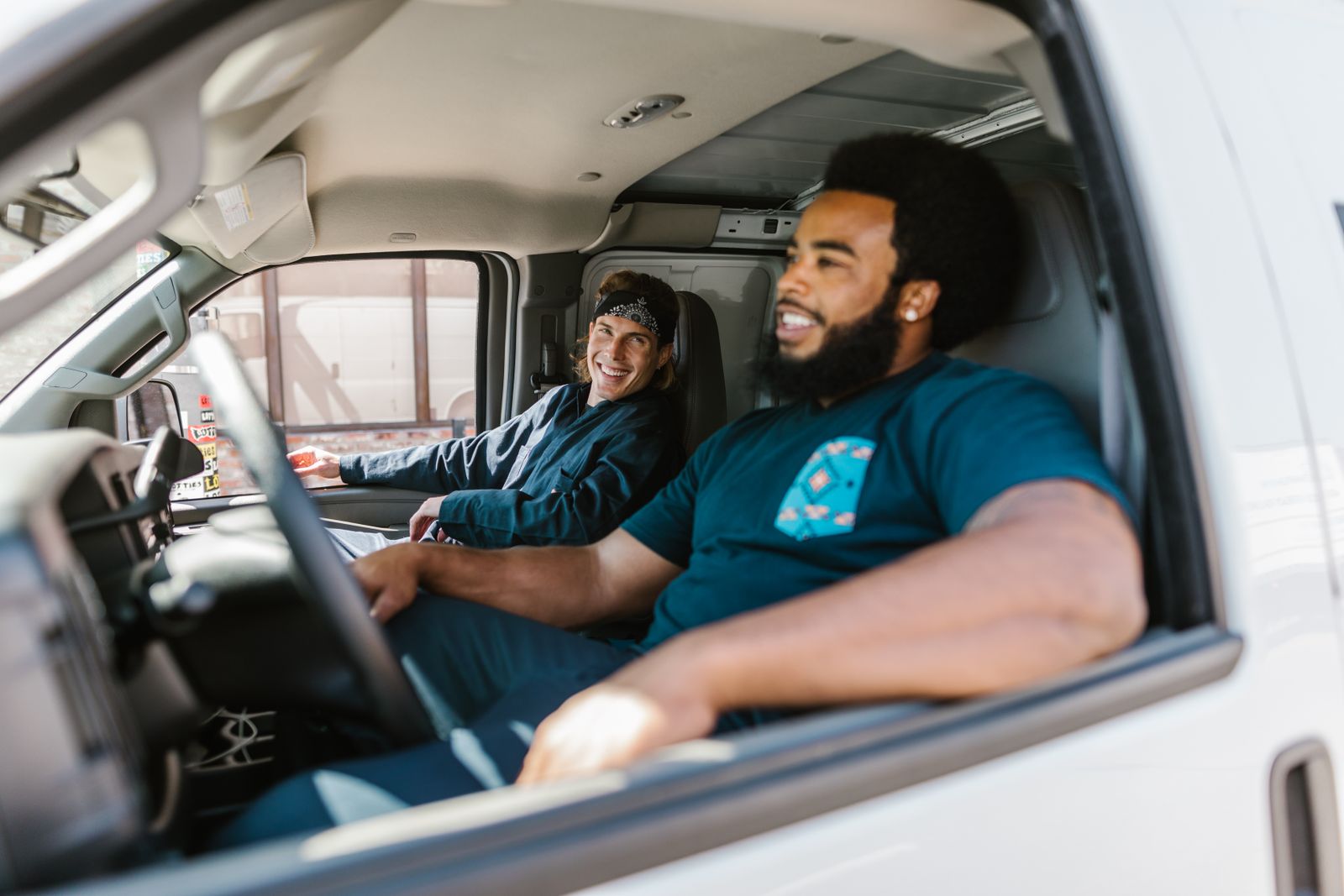 Two colleagues sitting in a van, smiling and relaxed, showcasing teamwork.