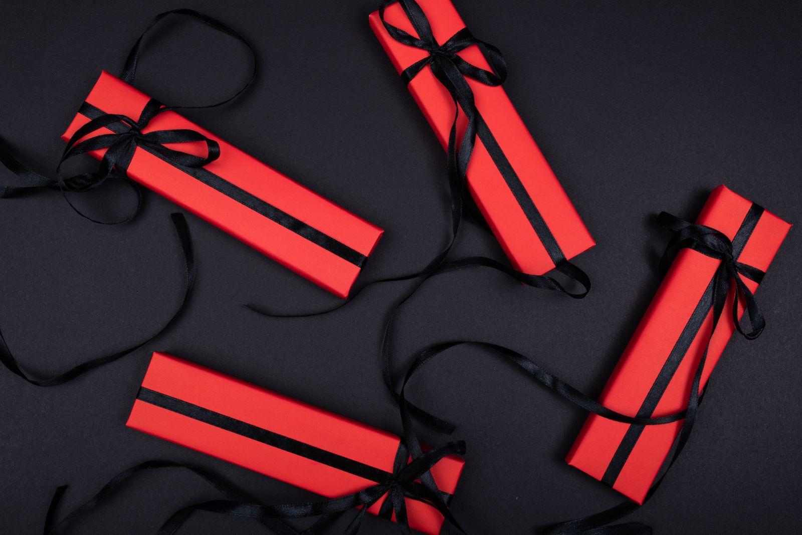 Top view of red gift boxes with black ribbons arranged on a black background.